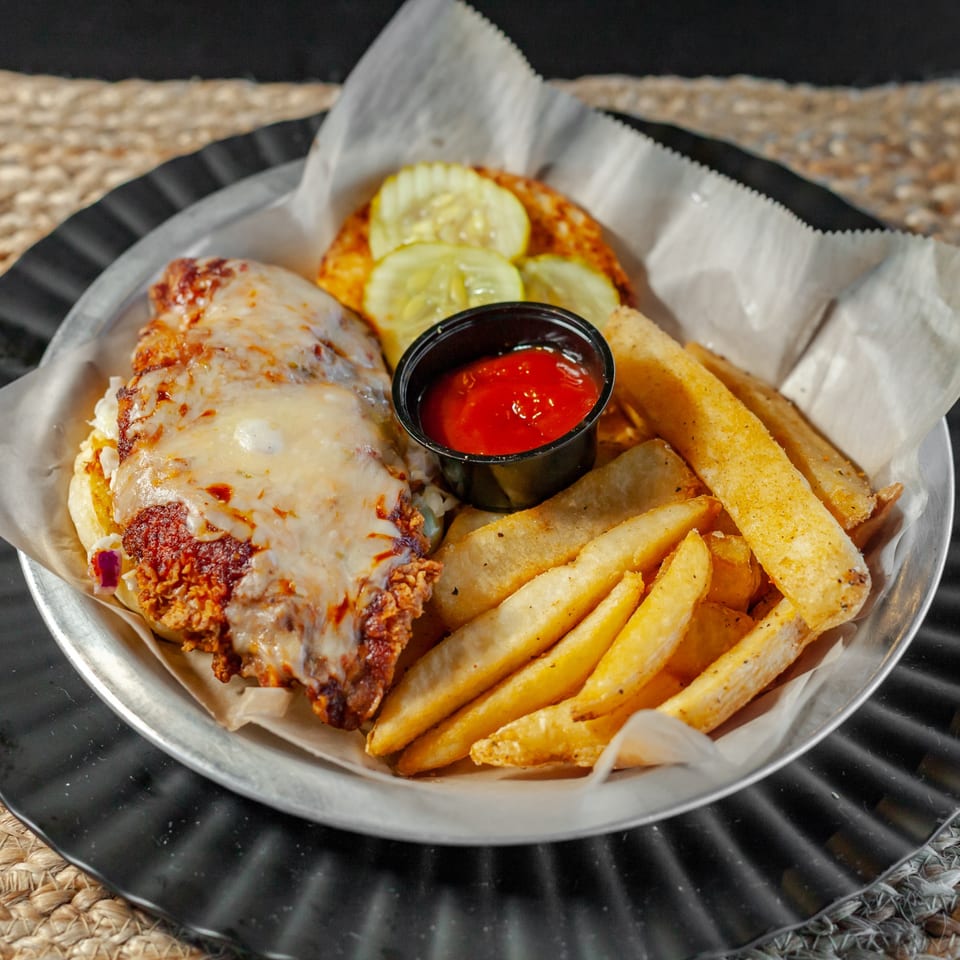 A Draft Sports Bar & Grill chicken sandwich with melted cheese, pickles, fries, and ketchup.