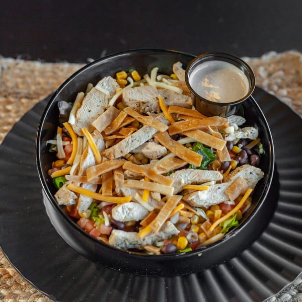 A black bowl of The Draft's chicken salad with tortilla strips, cheese, corn, and dressing.