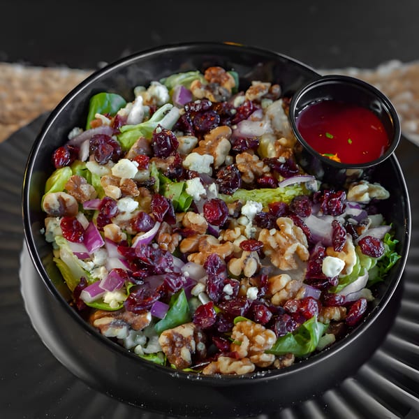 A vibrant salad with lettuce, walnuts, dried cranberries, red onion, and feta cheese, with a side of dressing.