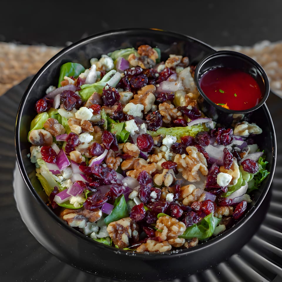 A vibrant salad with lettuce, walnuts, dried cranberries, red onion, and feta cheese, with a side of dressing.