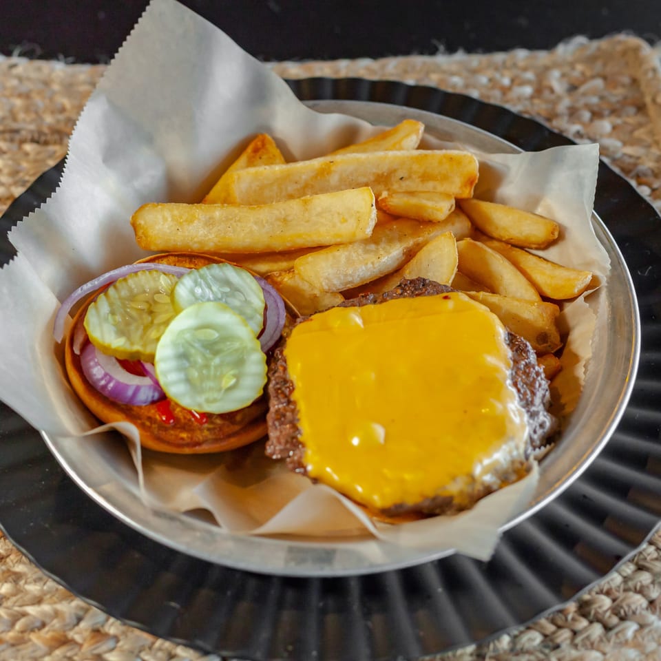 Cheeseburger with pickles, red onion, and fries in a metal basket at The Draft Sports Bar & Grill.