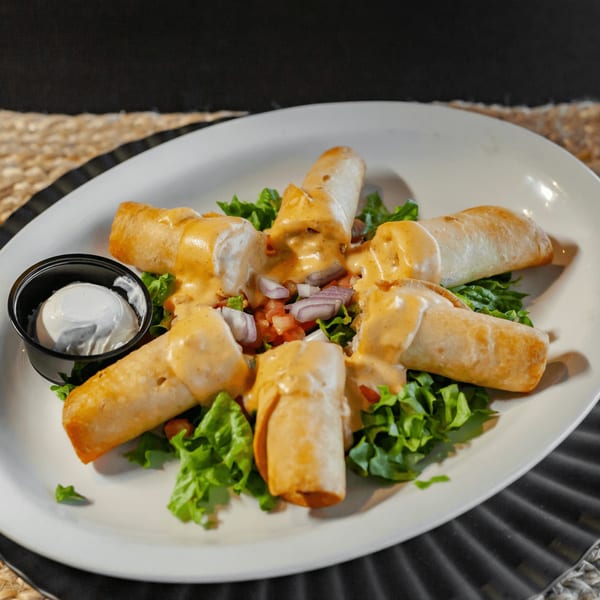 Taquitos from The Draft Sports Bar & Grill, topped with sauce, lettuce, pico de gallo, and a side of sour cream.