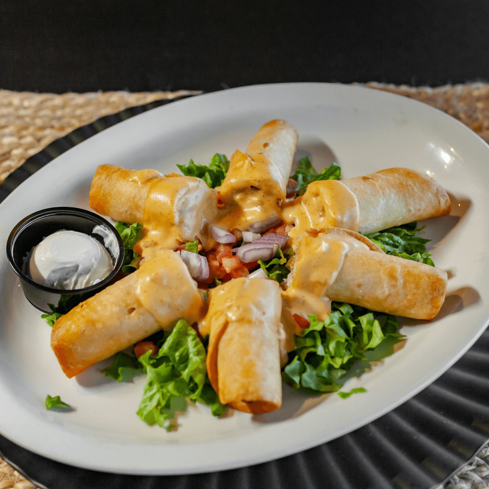 Taquitos from The Draft Sports Bar & Grill, topped with sauce, lettuce, pico de gallo, and a side of sour cream.