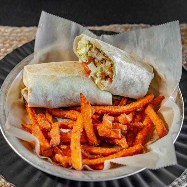 Two chicken wraps with lettuce, tomato, and sauce, served with a side of sweet potato fries.