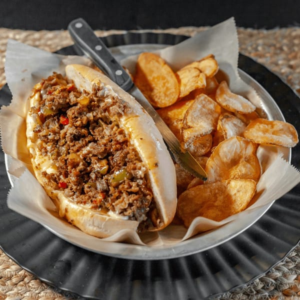 Cheesesteak sandwich with melted cheese, peppers, and onions, served with crispy potato chips.